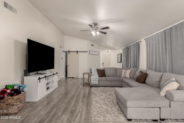 living room with a barn door, lofted ceiling, ceiling fan, and light hardwood / wood-style flooring