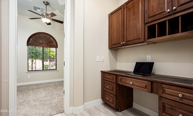 unfurnished office featuring ceiling fan, built in desk, and light hardwood / wood-style flooring