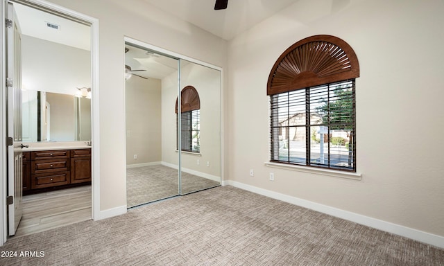 unfurnished bedroom featuring ensuite bath, ceiling fan, light carpet, and a closet