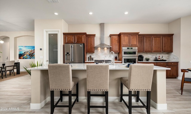 kitchen featuring appliances with stainless steel finishes, an island with sink, a breakfast bar area, and wall chimney range hood