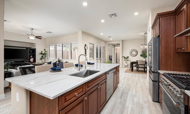 kitchen featuring light stone countertops, appliances with stainless steel finishes, light wood-type flooring, a kitchen island with sink, and sink