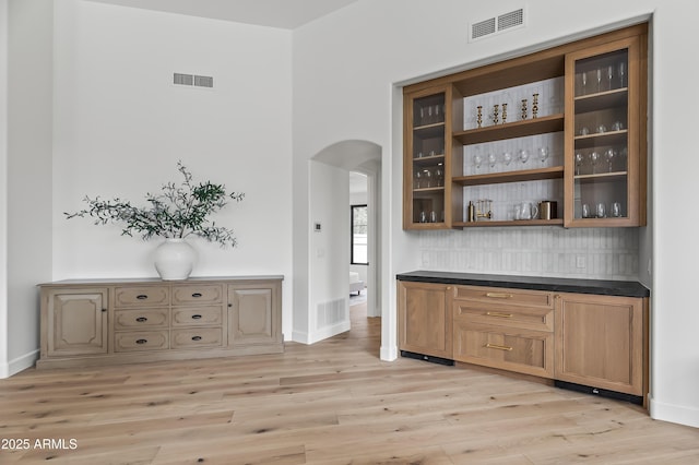 bar featuring visible vents, arched walkways, tasteful backsplash, and light wood-style flooring