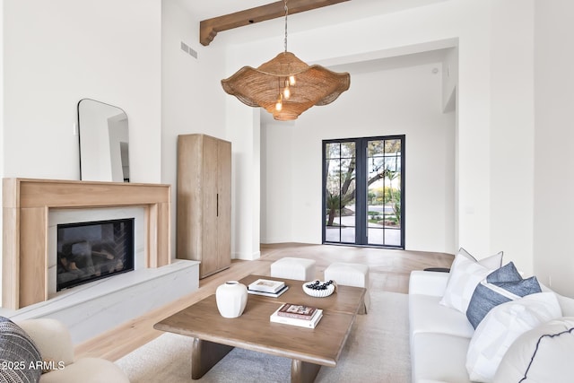 living room featuring visible vents, a premium fireplace, beam ceiling, a towering ceiling, and wood finished floors