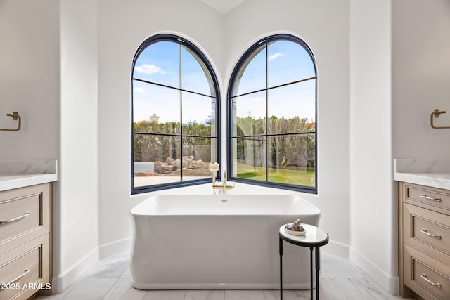 bathroom with marble finish floor, vanity, baseboards, and a freestanding tub