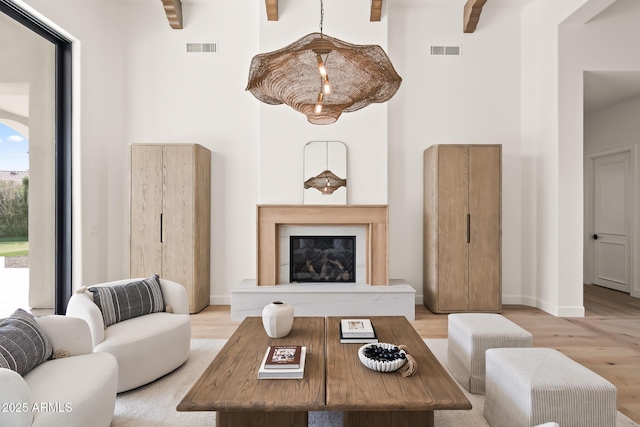 living room with a glass covered fireplace, visible vents, a high ceiling, and wood finished floors