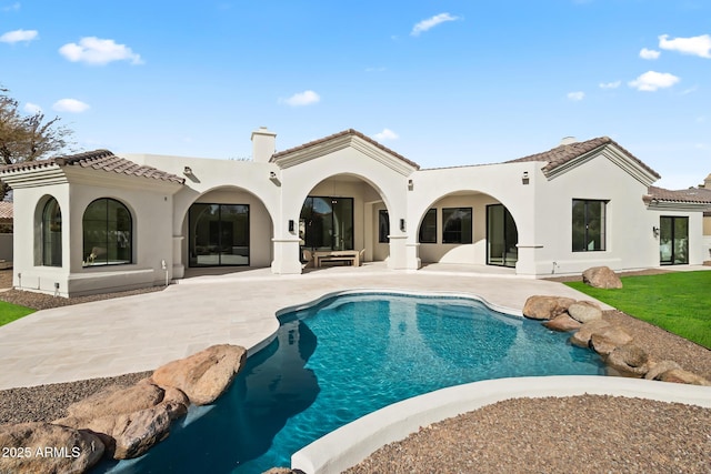 rear view of house with stucco siding, a tile roof, an outdoor pool, a chimney, and a patio area