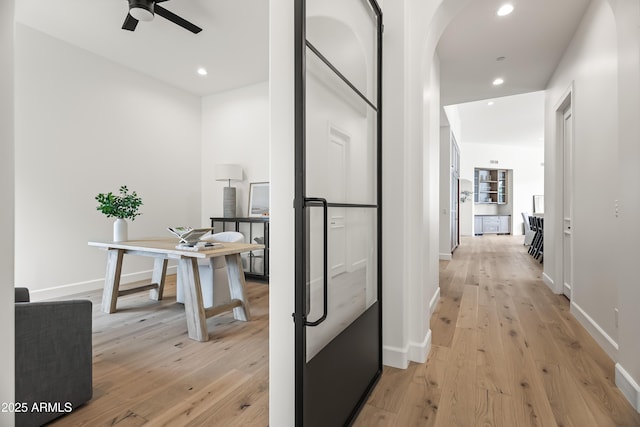 hall featuring arched walkways, recessed lighting, light wood-type flooring, and baseboards