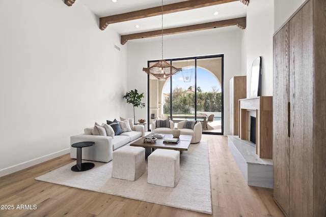 living area with beam ceiling, a fireplace with raised hearth, light wood-type flooring, and baseboards