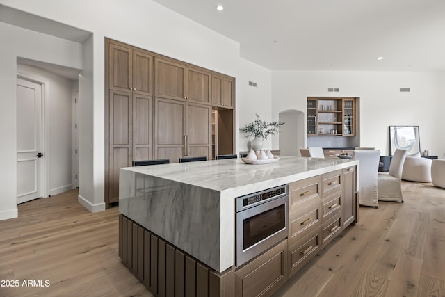 kitchen featuring recessed lighting, stainless steel microwave, arched walkways, and light wood finished floors