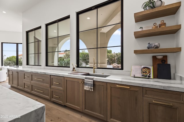 kitchen featuring a sink, open shelves, light stone counters, and light wood-style flooring