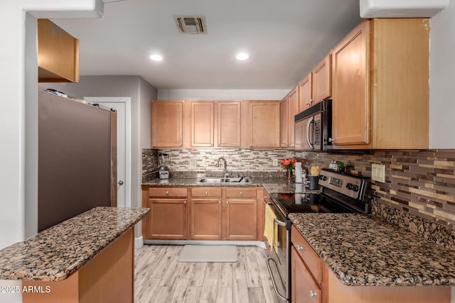 kitchen with light wood-type flooring, stainless steel appliances, sink, dark stone countertops, and decorative backsplash