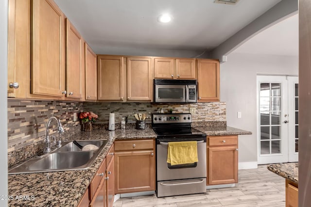 kitchen featuring sink, backsplash, light wood-type flooring, dark stone counters, and stainless steel appliances