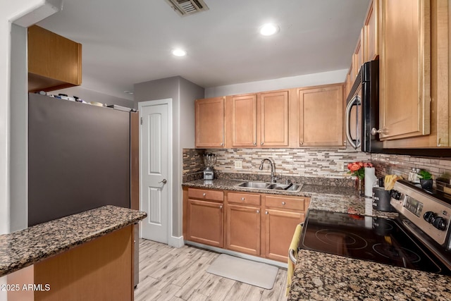 kitchen featuring tasteful backsplash, light wood-type flooring, stainless steel appliances, dark stone counters, and sink