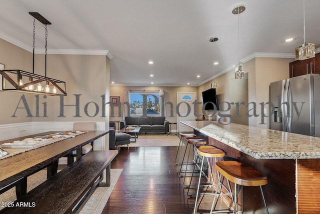 kitchen with a kitchen breakfast bar, hanging light fixtures, ornamental molding, light stone counters, and stainless steel refrigerator with ice dispenser