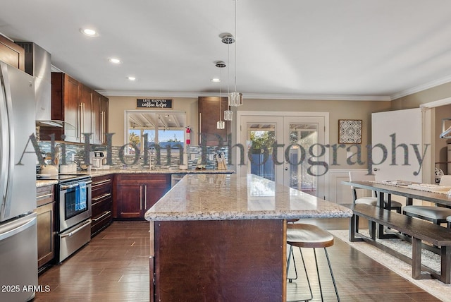 kitchen featuring a kitchen island, appliances with stainless steel finishes, hanging light fixtures, a healthy amount of sunlight, and wall chimney exhaust hood