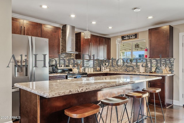 kitchen with pendant lighting, a breakfast bar area, appliances with stainless steel finishes, a center island, and wall chimney exhaust hood