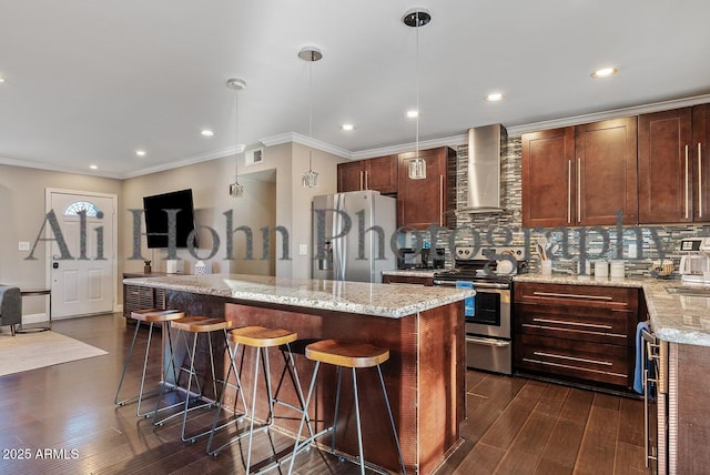 kitchen with light stone counters, decorative light fixtures, a kitchen island, stainless steel appliances, and wall chimney range hood