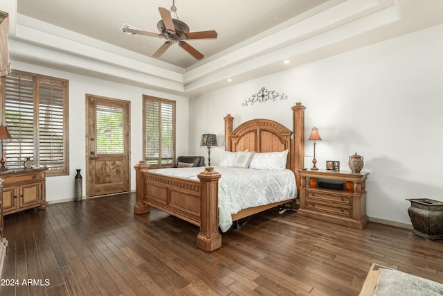 bedroom with ceiling fan, dark hardwood / wood-style floors, and a tray ceiling