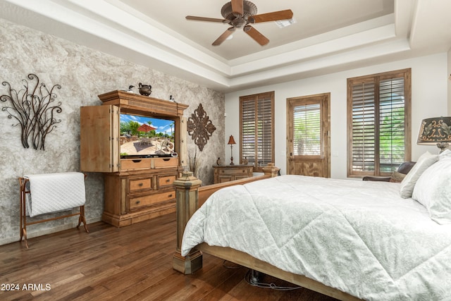 bedroom with ceiling fan, dark hardwood / wood-style floors, and a raised ceiling