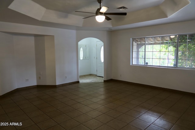 tiled empty room with ceiling fan and a tray ceiling