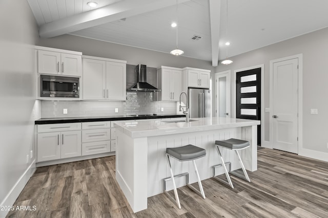 kitchen with an island with sink, sink, white cabinets, stainless steel appliances, and wall chimney exhaust hood