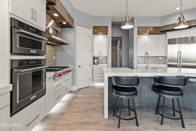 kitchen with a kitchen bar, sink, white cabinetry, hanging light fixtures, and stainless steel appliances