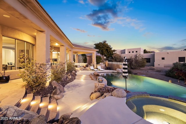 pool at dusk with an in ground hot tub and a patio area