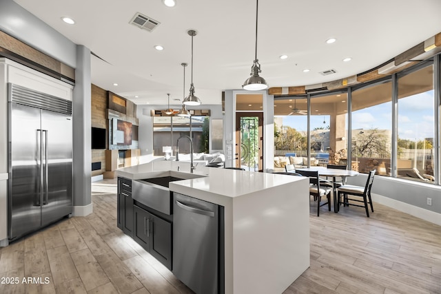 kitchen featuring pendant lighting, sink, light hardwood / wood-style flooring, appliances with stainless steel finishes, and a kitchen island with sink