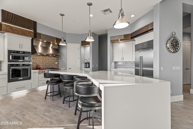 kitchen featuring appliances with stainless steel finishes, a kitchen island with sink, white cabinetry, a kitchen breakfast bar, and light wood-type flooring