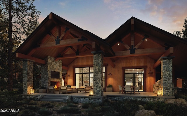 rear view of house with a patio area, an outdoor living space with a fireplace, and stone siding