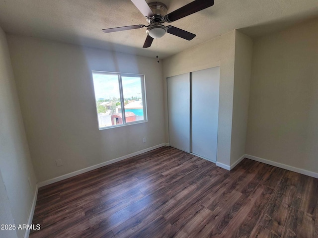 unfurnished bedroom featuring a textured ceiling, a ceiling fan, baseboards, a closet, and dark wood-style floors