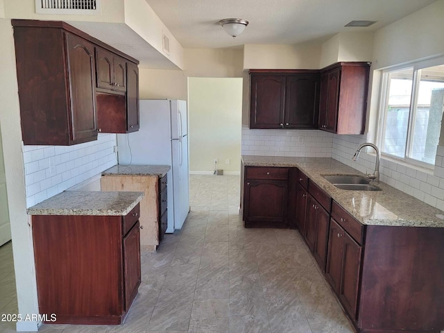 kitchen with light stone counters, tasteful backsplash, a sink, and visible vents