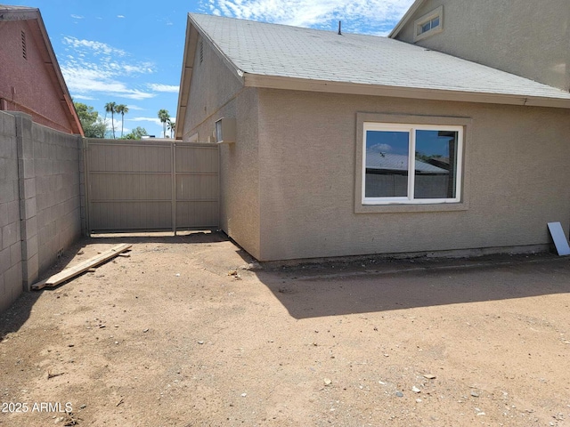 view of side of home with roof with shingles, fence, and stucco siding