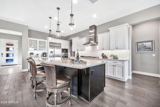 kitchen with white cabinets, a center island with sink, stainless steel appliances, and wall chimney exhaust hood