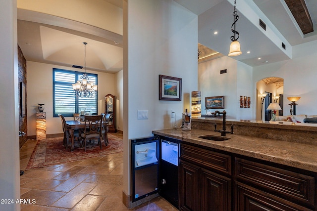 kitchen featuring dark brown cabinetry, sink, an inviting chandelier, dark stone countertops, and pendant lighting