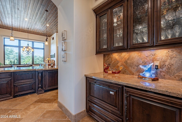 bar featuring dark brown cabinetry, light stone counters, hanging light fixtures, wooden ceiling, and backsplash