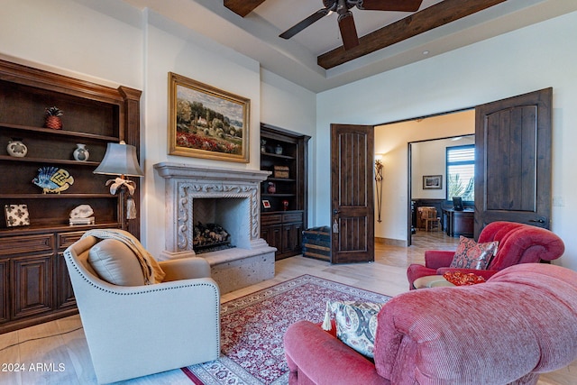 living room featuring beamed ceiling, ceiling fan, a fireplace, and light wood-type flooring