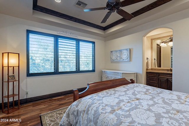 bedroom with dark wood-type flooring, ensuite bathroom, crown molding, a raised ceiling, and ceiling fan