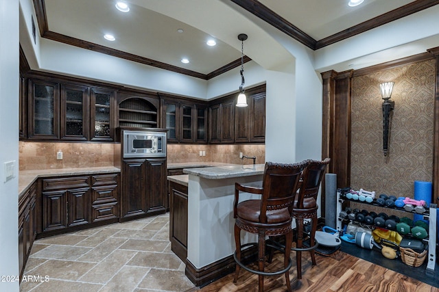 kitchen with stainless steel microwave, hanging light fixtures, crown molding, light stone countertops, and dark brown cabinets