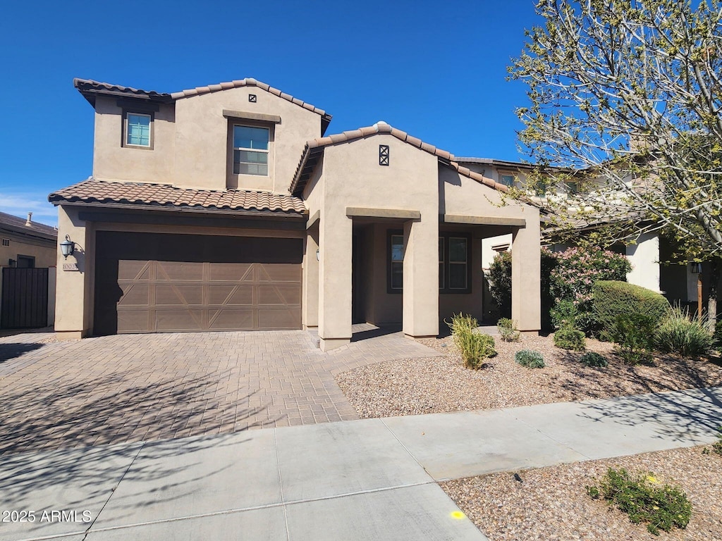 mediterranean / spanish-style house with a tile roof, decorative driveway, a garage, and stucco siding