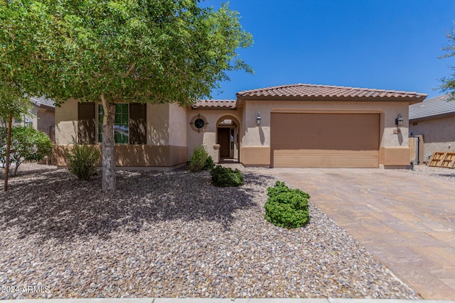 mediterranean / spanish home with a garage, decorative driveway, a tiled roof, and stucco siding