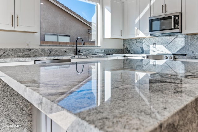 kitchen featuring tasteful backsplash, white cabinets, stainless steel microwave, and light stone countertops