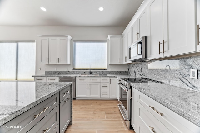 kitchen featuring recessed lighting, stainless steel appliances, white cabinetry, light stone countertops, and light wood finished floors