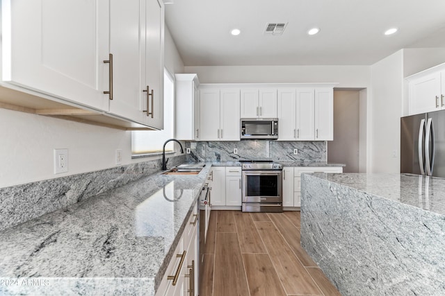 kitchen with visible vents, appliances with stainless steel finishes, light stone countertops, white cabinetry, and a sink