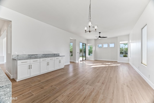 unfurnished living room featuring ceiling fan with notable chandelier, light wood-style flooring, and baseboards