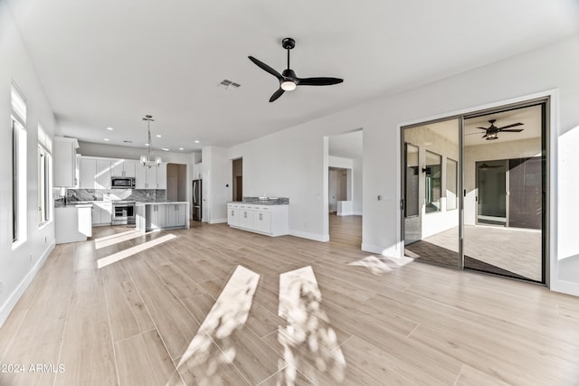 unfurnished living room featuring ceiling fan with notable chandelier, light wood-style flooring, visible vents, and baseboards