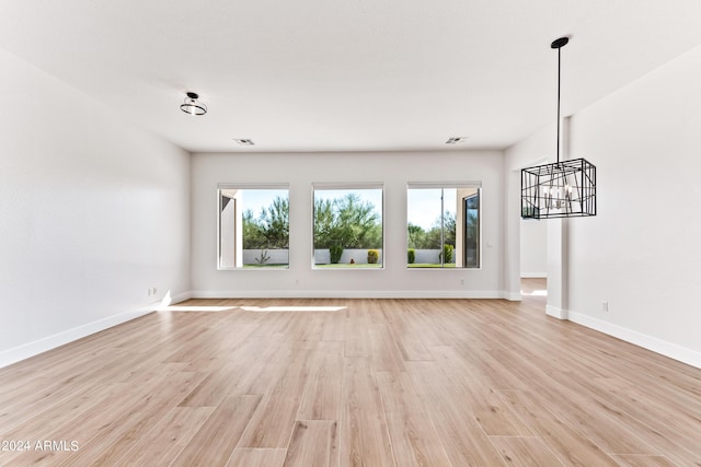 unfurnished living room featuring light wood-style floors, baseboards, and an inviting chandelier