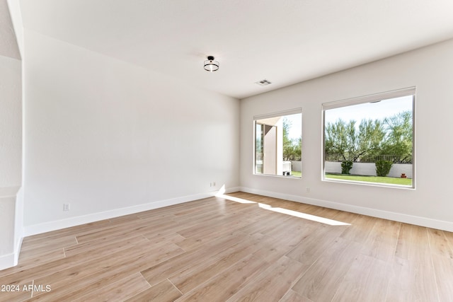 empty room with baseboards, visible vents, and light wood finished floors