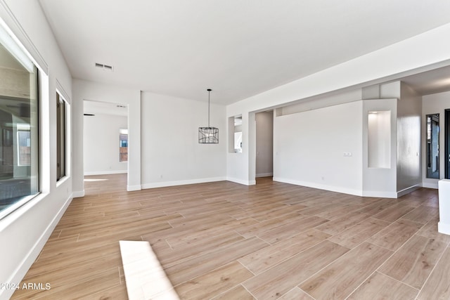 unfurnished living room with a chandelier, visible vents, light wood-style flooring, and baseboards