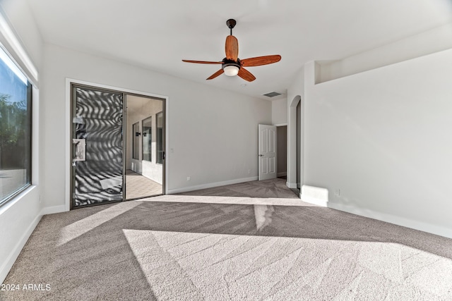 carpeted empty room featuring arched walkways, a ceiling fan, visible vents, and baseboards